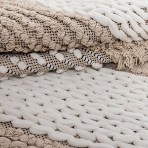 May include: A close-up of a beige and white woven rug with a textured pattern. The rug is made of natural fibers and has a soft, cozy feel.