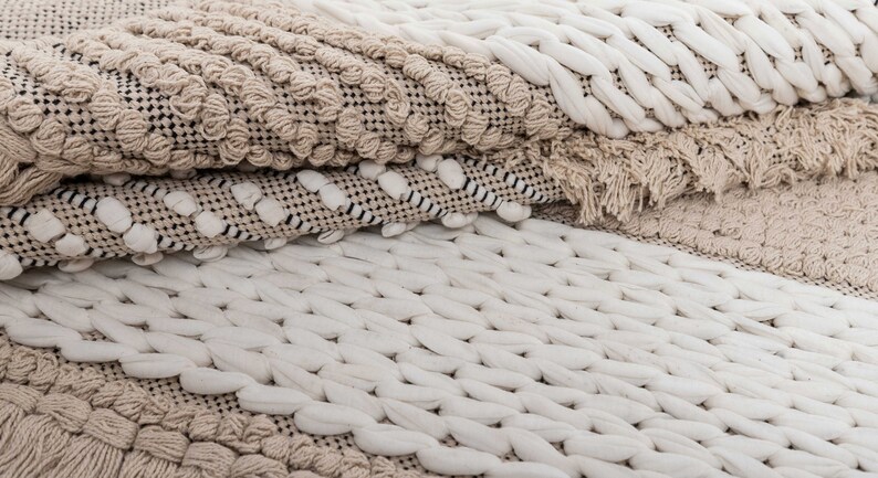 May include: A close-up of a beige and white woven rug with a textured pattern. The rug is made of natural fibers and has a soft, cozy feel.