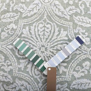 May include: A close-up of a light gray patterned rug with two color swatches. One swatch is a range of green shades and the other is a range of blue shades.
