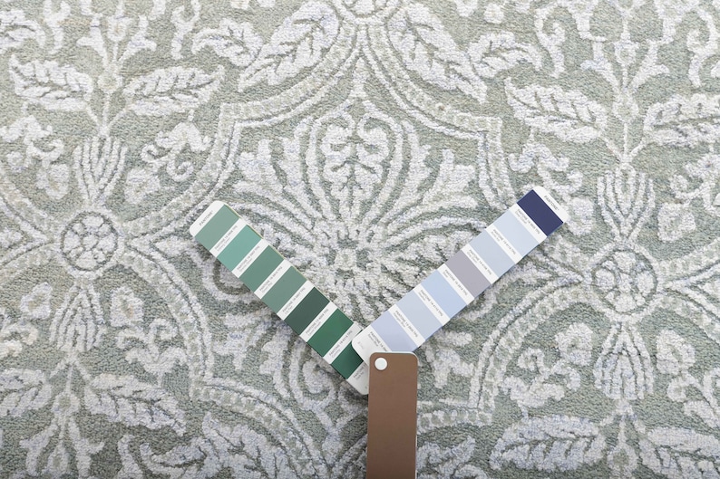 May include: A close-up of a light gray patterned rug with two color swatches. One swatch is a range of green shades and the other is a range of blue shades.