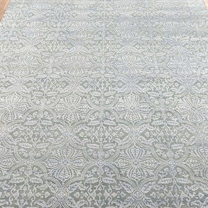 May include: A light gray area rug with a white, intricate, floral pattern. The rug has a subtle sheen and a soft, plush texture.