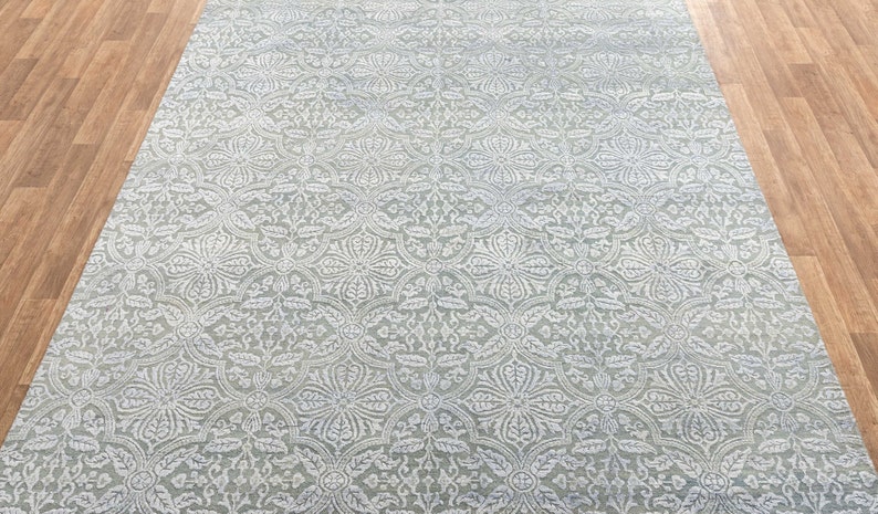 May include: A light gray area rug with a white, intricate, floral pattern. The rug has a subtle sheen and a soft, plush texture.