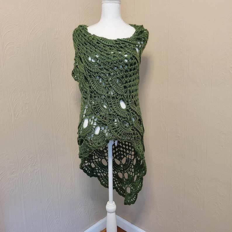 May include: A green crocheted shawl with a high-low hemline. The shawl is made with a delicate openwork stitch and has a flowing, asymmetrical design.