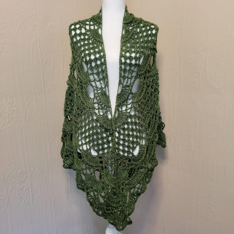 May include: A green crocheted shawl with a delicate lace pattern. The shawl is draped over a mannequin and has a triangular shape.