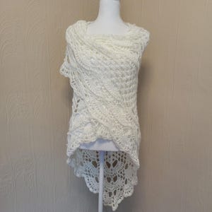 Puede incluir: Chale de ganchillo blanco con un dobladillo alto-bajo. El chal está hecho con un delicado patrón de calado y tiene un borde festoneado.
