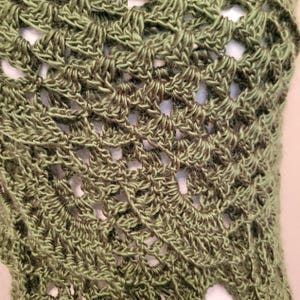 May include: A green crocheted shawl with a delicate, lacy pattern. The shawl is made with a soft, lightweight yarn and has a flowing, drapey design.