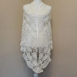 May include: White crocheted shawl with a delicate lace pattern. The shawl is draped over a white mannequin.
