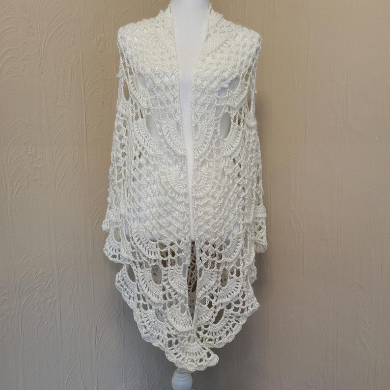May include: White crocheted shawl with a delicate lace pattern. The shawl is draped over a white mannequin.