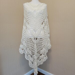 May include: White crochet shawl with a delicate lace pattern. The shawl is draped over a mannequin and has a scalloped edge.