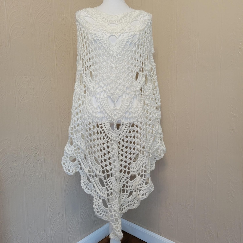 May include: White crochet shawl with a delicate lace pattern. The shawl is draped over a mannequin and has a scalloped edge.