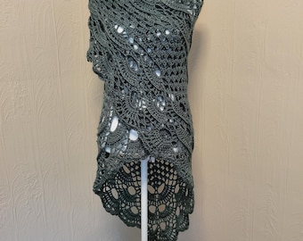 May include: A green crocheted shawl with a high-low hemline. The shawl is made with a delicate openwork pattern and has a scalloped edge.
