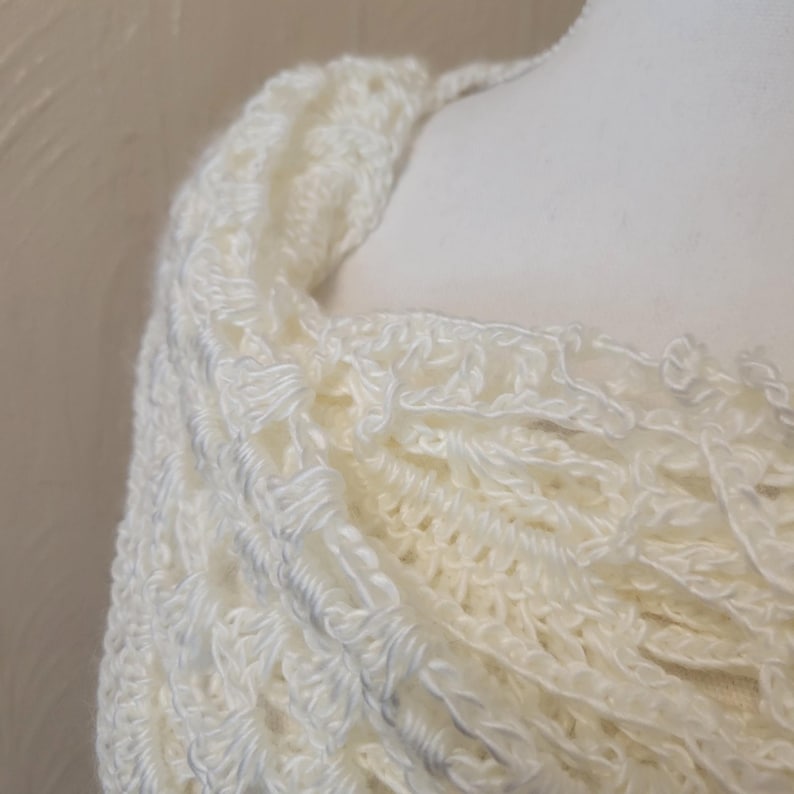 May include: A white crocheted shawl with a delicate, lacy pattern. The shawl is draped over a mannequin's shoulders, showcasing its soft and flowing texture.