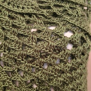 May include: Close-up of a green crocheted shawl with a lacy pattern.