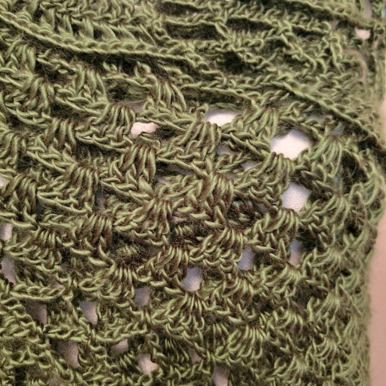 May include: Close-up of a green crocheted shawl with a lacy pattern.