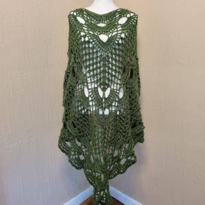 May include: A green crochet shawl with a delicate lace pattern. The shawl is draped over a mannequin and has a scalloped edge.