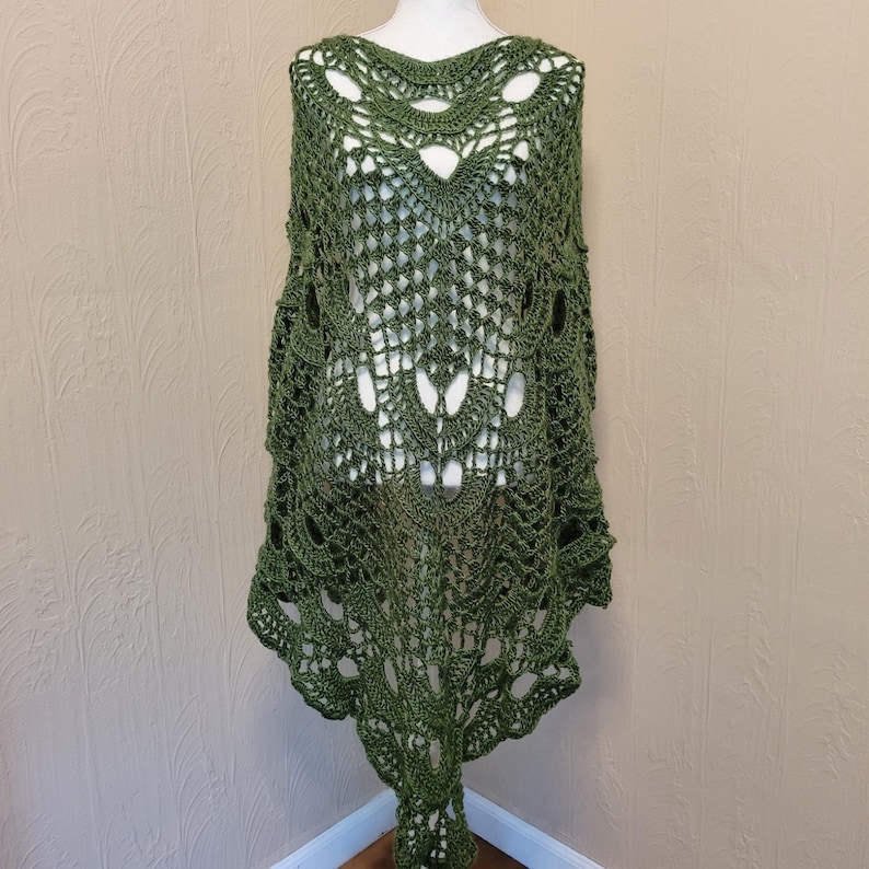 May include: A green crochet shawl with a delicate lace pattern. The shawl is draped over a mannequin and has a scalloped edge.