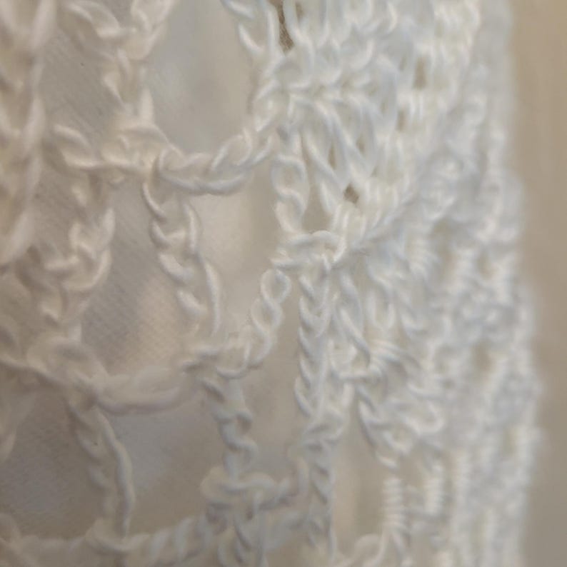 May include: White crochet fabric with a delicate, intricate pattern. The fabric is soft and airy, with a slightly textured surface.