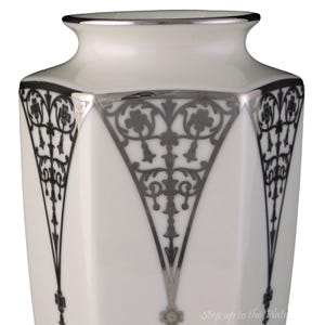 Puede incluir: Jarr&oacute;n de porcelana blanca con un dise&ntilde;o geom&eacute;trico plateado. El jarr&oacute;n tiene una forma hexagonal y un borde plateado.