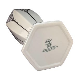 Puede incluir: Jarr&oacute;n de cer&aacute;mica blanca con base hexagonal. El jarr&oacute;n est&aacute; decorado con un dise&ntilde;o en negro y plata y tiene el texto "LENOX CENTENNIAL 1689-1989 XONE A Lenox Limited Edition. Hand-Engraved and Decorated with Sterling Silver" en la parte inferior.