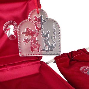 May include: A clear glass Christmas ornament featuring Mickey Mouse and Pluto. The ornament is shaped like a heart and has the year 1999 etched on the side. The ornament is in a red velvet box.