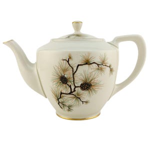 May include: Cream-colored ceramic teapot with a lid and handle. The teapot is decorated with a pine branch design featuring brown pinecones and green and gold needles. Gold trim accents the spout, lid, and base.