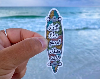 May include: A colorful skateboard sticker with the text "Let the good vibes roll" on a white background. The sticker is being held in front of a beach scene.