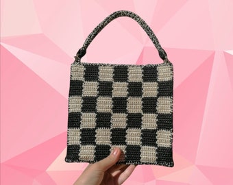 Könnte beinhalten: Eine kleine, gehäkelte Handtasche mit schwarzem und weißem Karomuster und einem einzigen Henkel oben.
