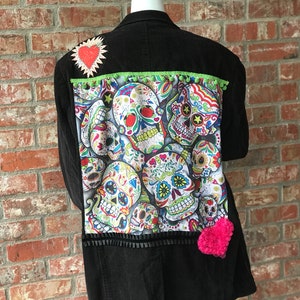May include: Black corduroy jacket with a colorful sugar skull design on the back. The jacket has green trim and two pink felt hearts.