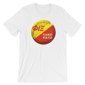 Puede incluir: Camiseta blanca con un gráfico circular rojo y amarillo con el texto "ΦΙΕ" y "KANEI KALO".