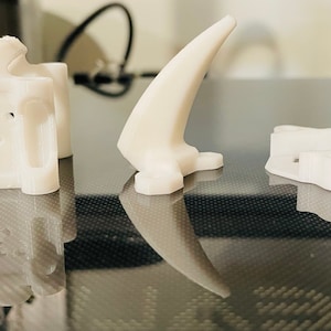 May include: Three white 3D printed plastic objects. The objects are on a black surface. The objects are different shapes and sizes.