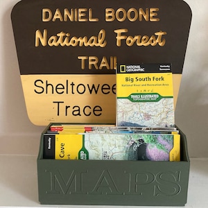 May include: A green box with the word "MAPS" embossed on the front, holding a stack of folded maps. The maps are for the Daniel Boone National Forest, Sheltowee Trace, and Big South Fork National River and Recreation Area.