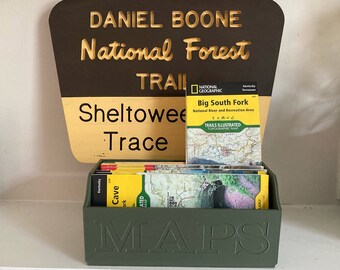 May include: A green box with the word "MAPS" embossed on the front, holding a stack of folded maps. The maps are for the Daniel Boone National Forest, Sheltowee Trace, and Big South Fork National River and Recreation Area.