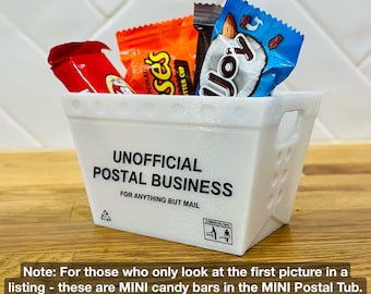 May include: A white, rectangular container with the text "UNOFFICIAL POSTAL BUSINESS" holds mini candy bars. The container is 3 3/4 inches wide, 2 1/2 inches deep, and 2 1/2 inches tall. Candy bar wrappers are red, orange, brown, and blue.