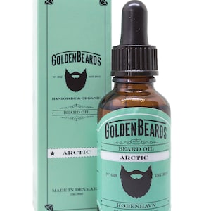 Op de afbeelding: Een groen-witte doos en een bruine glazen fles met een druppelaar. De fles en de doos hebben beide een etiket met de tekst "Golden Beards Beard Oil Arctic" en een afbeelding van een baard. De doos vermeldt ook "Handmade & Organic" en "Made in Denmark".