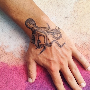 May include: A temporary tattoo of a black octopus with eight tentacles on a person's wrist.