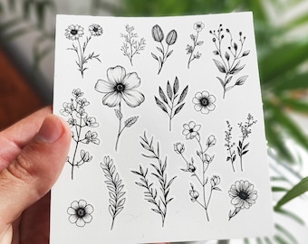 May include: A sheet of black and white floral stickers featuring various flowers, leaves, and stems. The stickers are perfect for adding a touch of nature to journals, planners, and other craft projects.