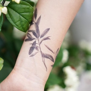 Könnte beinhalten: Ein schwarz-weißes temporäres Tattoo eines belaubten Zweigs auf dem Handgelenk einer Person.