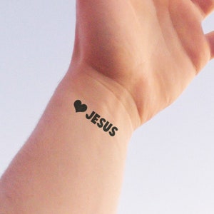 May include: A person's wrist with a black heart and the word "JESUS" tattooed on it.