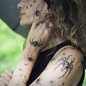 May include: A person with multiple spider temporary tattoos on their face, arms, and shoulders. The tattoos are black and range in size.