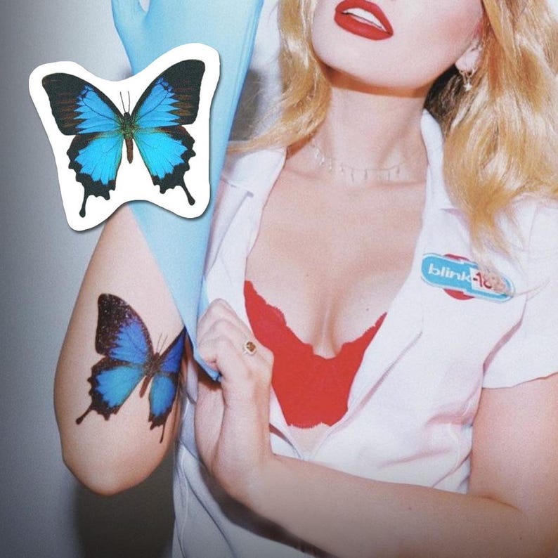May include: A woman wearing a white uniform with a red bra underneath and a blue butterfly tattoo on her arm. The uniform has a name tag that says "blink-182".