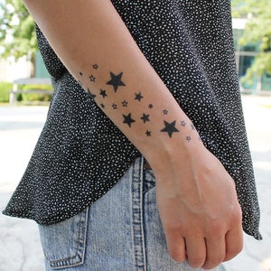 May include: A person's arm with a temporary tattoo of black stars of different sizes.