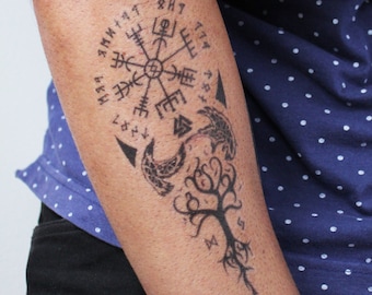 May include: A black and white tattoo design on a person's arm. The design features a compass with runes, a tree of life, and two birds.