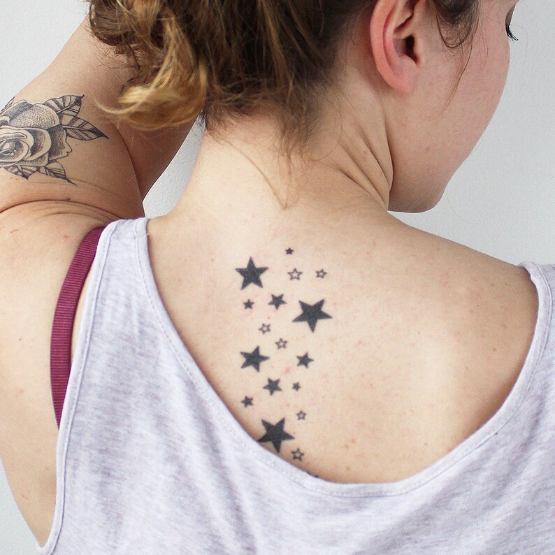 May include: A woman with a rose tattoo on her arm has a small tattoo of a cluster of stars on her back.
