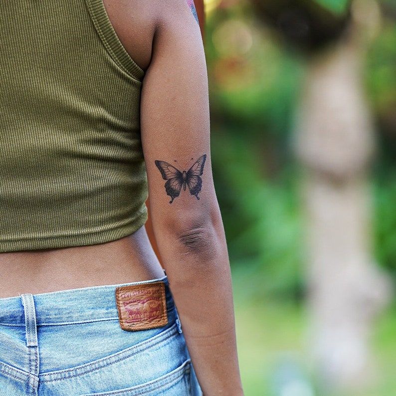 May include: A person's arm with a black butterfly temporary tattoo on the elbow.