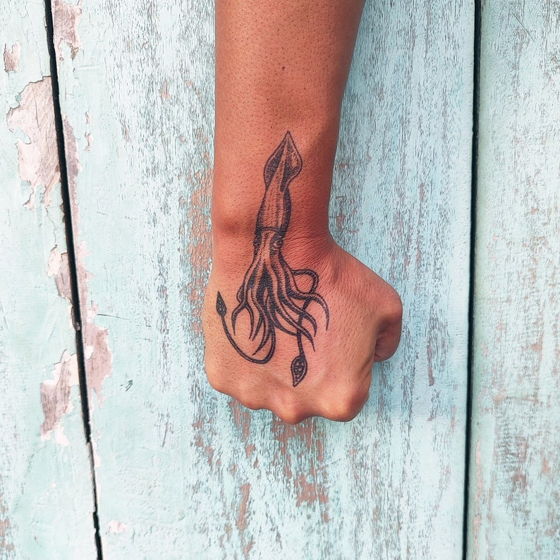 Puede incluir: Un tatuaje en blanco y negro de un calamar en la mu&ntilde;eca de una persona.