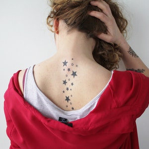 May include: A woman with curly brown hair has a tattoo of a line of stars down the back of her neck.