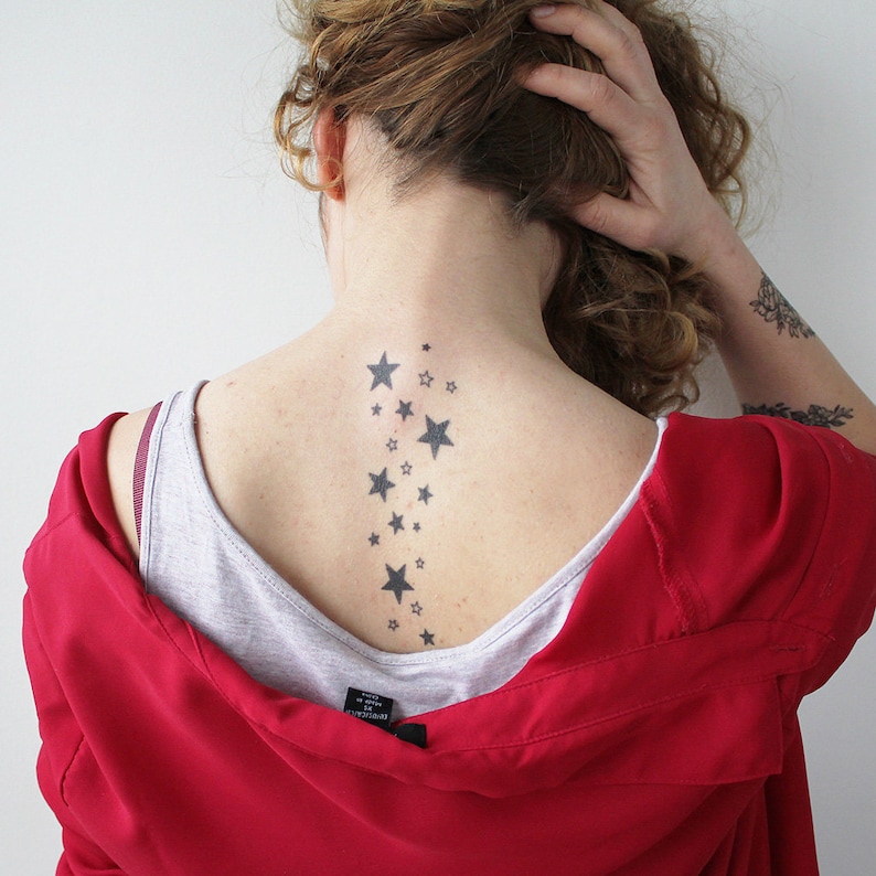 May include: A woman with curly brown hair has a tattoo of a line of stars down the back of her neck.