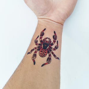May include: A red and black spider tattoo on a person's wrist.