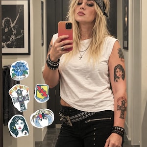May include: A collection of five embroidered patches featuring a blue rose with the text Axl Rose, a cross with skulls and the text Guns N' Roses, a shield with a red branch, a portrait of a woman with a rose, and a winged emblem with the text Rocker.