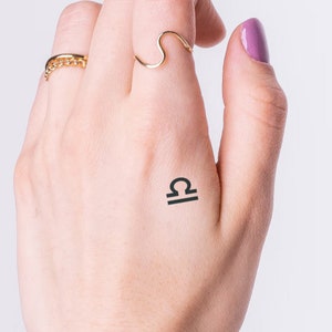 May include: A temporary tattoo of the Libra zodiac symbol on a person's hand.